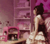 a girl in a pink dress is standing in front of a pink dollhouse .