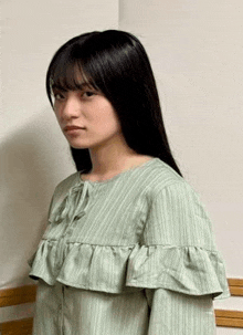 a young woman wearing a green ruffled dress is standing in front of a wall .