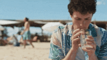 a man in a hawaiian shirt is drinking from a glass on the beach