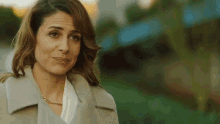a woman wearing a white shirt and a tan coat is looking at the camera .