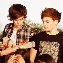 harry styles and louis tomlinson are standing next to each other holding a gift box