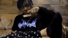 a man with blue hair is sitting on a couch holding a remote control .