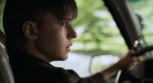 a young man is driving a car and looking out the window