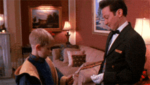 a man in a tuxedo is standing next to a boy in a living room