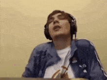 a man wearing headphones and a blue jacket is sitting at a table with his eyes closed .