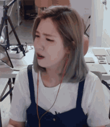 a woman wearing a white shirt and blue overalls is sitting in front of a table