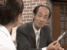 a man in a suit and tie is talking to a woman in front of a brick wall with the letter z on it