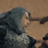 a man with gray hair and a beard is wearing armor and a ponytail