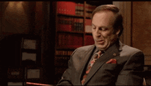 a man in a suit and tie is sitting in front of a bookshelf with books on it .