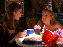 two women sitting at a table with a birthday hat on their head