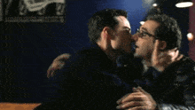 two men are kissing in front of a sign that says ' a ' on it .