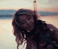 a woman is playing a violin in front of a lake