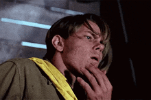 a man with a yellow scarf around his neck is touching his face .
