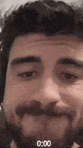 a close up of a man 's face with a beard and headphones with the time 0:00 on the bottom
