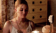 a woman in a white tank top is sitting at a table with a candle in front of her .