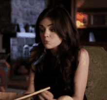 a woman is sitting on a couch eating with chopsticks and making a funny face