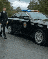 a man in a uniform walks past a police car that says bamom