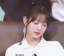 a woman is sitting on a couch with her eyes closed . she is wearing a white shirt and earrings .