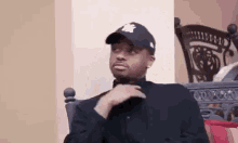 a man is sitting in a chair wearing a baseball cap and adjusting his tie .