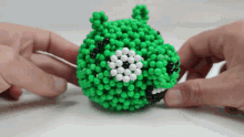 a person is holding a green angry bird made out of green and white beads