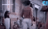 a man without a shirt is standing next to a woman in a white dress in a crowded area .