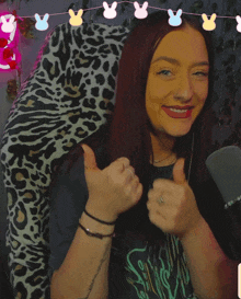 a woman giving a thumbs up with a leopard print blanket behind her