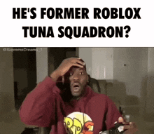 a man in a red hoodie is holding a video game controller and making a funny face while playing roblox .