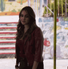 a woman in a red leather jacket is standing in front of a wall with stairs