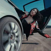 a woman in a race suit is laying on the ground next to a silver car