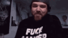 a man with a beard and a hat is wearing a black t-shirt that says `` fuck '' .