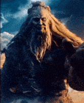 a giant with long hair and a beard is reaching out towards a person .