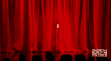 a woman in a white dress is standing in front of a red curtain .