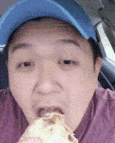 a man wearing a blue hat is eating a sandwich in a car