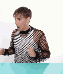 a man wearing a black and white fishnet shirt is making a surprised face