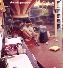 a man sits on a bench in a room with the name monikagoswamirk on the bottom