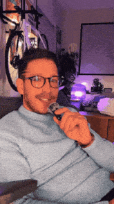 a man wearing glasses and a blue sweater holds a microphone