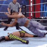 a woman is laying on the ground in a wrestling ring with a referee standing behind her .