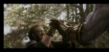 captain america and thanos are holding hands in a forest