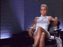 a woman in a white dress is sitting on a chair with her legs crossed