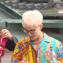 a man wearing glasses and a colorful shirt is holding a bottle .