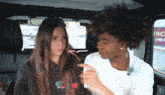 two girls are sitting in the back seat of a car talking to each other