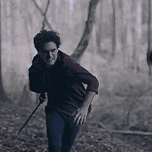 a man is holding a sword in the woods and looking at the camera .