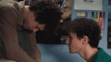 two young men looking at each other in front of a wall with a poster that says ' posters ' on it