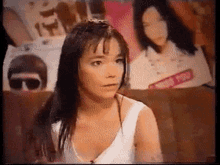 a woman in a white tank top stands in front of a poster that says i miss you