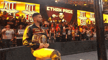 a wrestler is kneeling down in front of a crowd and holding a championship belt with the name ethan page behind him