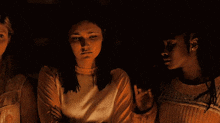 three women are standing next to each other in the dark .