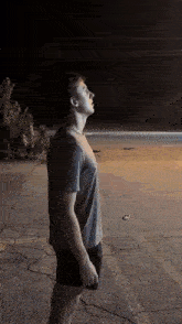 a man in a grey shirt and black shorts is standing in a dark parking lot looking up