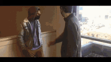 a man wearing a mask talks to another man in a room