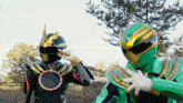 a man in a black and gold costume with a red circle on his chest is standing next to another man in a green costume