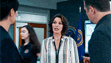 a woman in a striped shirt is talking to two men in a room with a flag in the background .